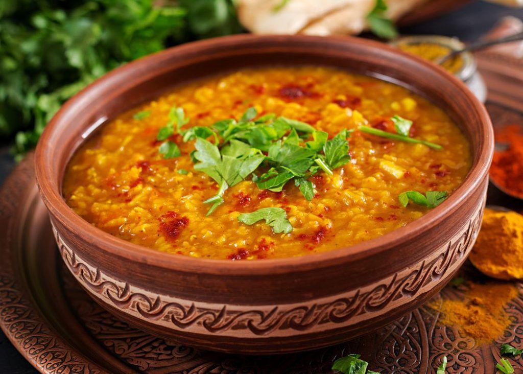Bowl of traditional lentil dal garnished with sliced green onions, served as part of a South Asian meal.