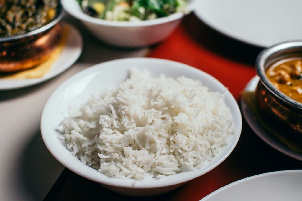 Steamed white rice served on a traditional metal platter alongside lentil soup and cooked leafy greens.